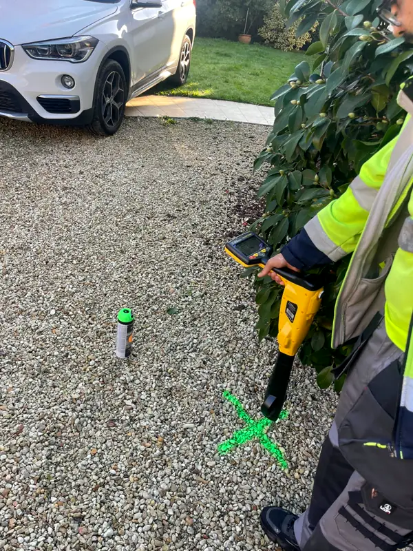 Technicien LOC RÉSEAU avec son détecteur de réseaux dans une allée de gravier, une croix verte peinte au sol