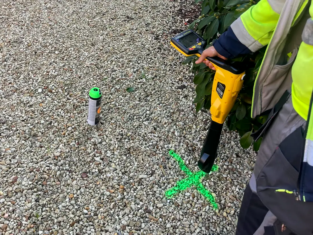Technicien LOC RÉSEAU avec son détecteur de réseaux, au-dessus d'une croix verte peinte sur le gravier